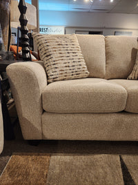 A beige Superstyle 5101 Loveseat with patterned cushions is beside a dark lamp and side table in the showroom.