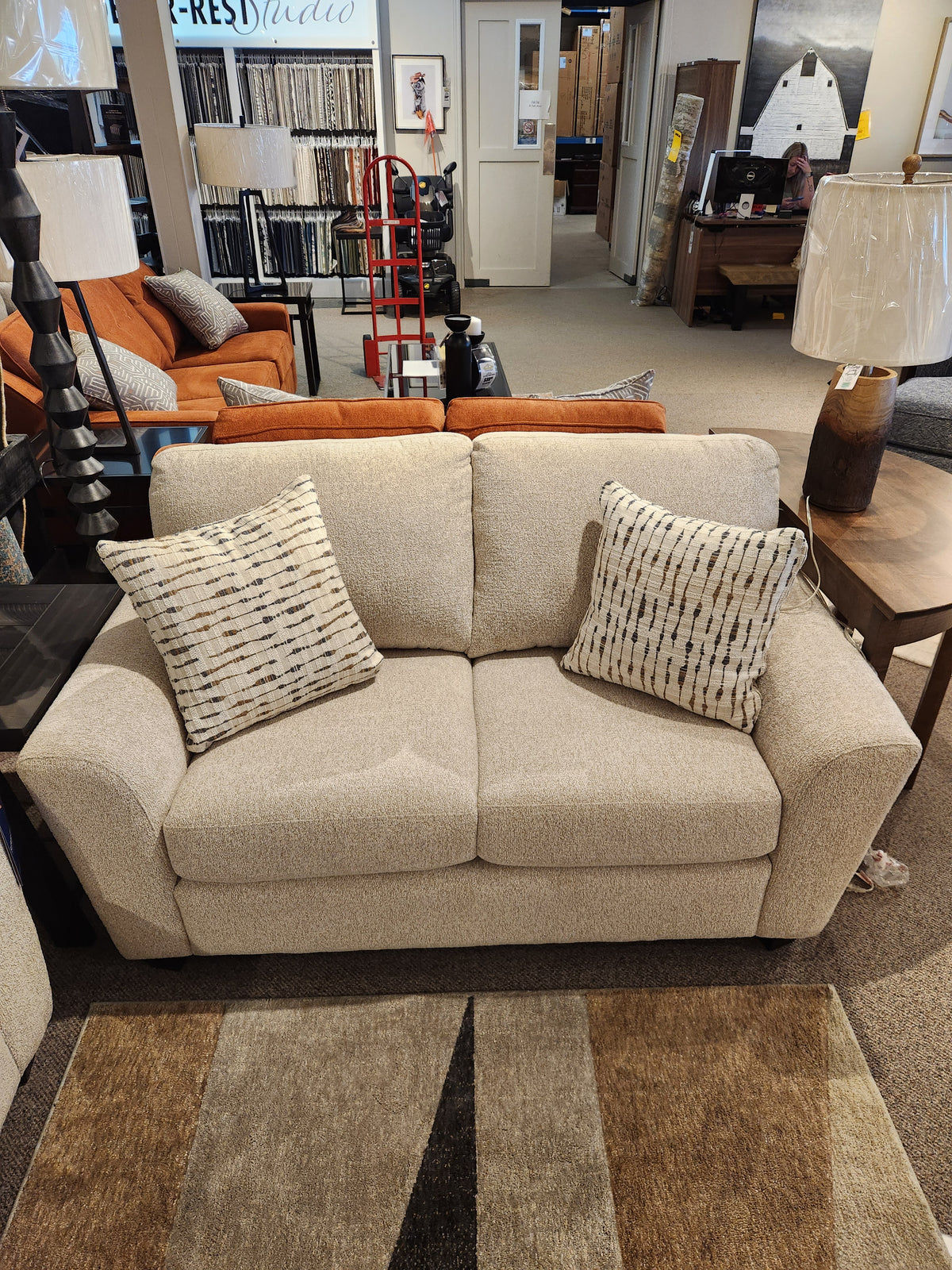 Superstyle 5101 Loveseat in beige upholstery with two patterned pillows, shown in a furniture showroom.