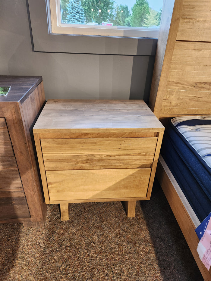 Handstone JA12 Jasper Nightstand in light wood, displayed between a bed and another piece in the showroom.