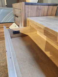 An open Handstone JA12 Jasper Nightstand drawer is shown beside a bed in a cozy, furnished room.