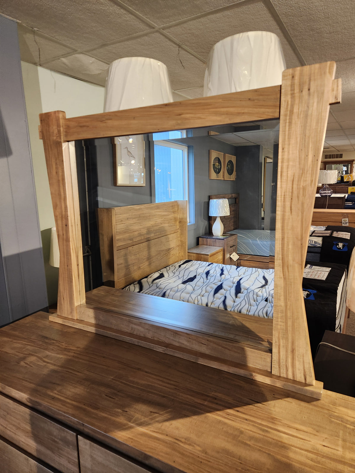 The Handstone JA9 Dresser Mirror reflects a bed and lamps in a showroom, displayed atop a dresser.