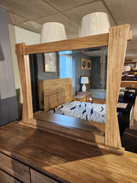 The Handstone JA9 Dresser Mirror reflects a bed and lamps in a showroom, displayed atop a dresser.