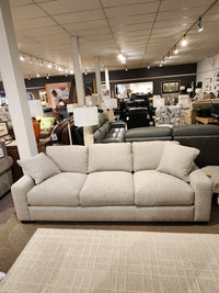 The Donald Choi Laguna Sofa has high-density foam seats, beige fabric, and two pillows, shown in a furniture showroom.