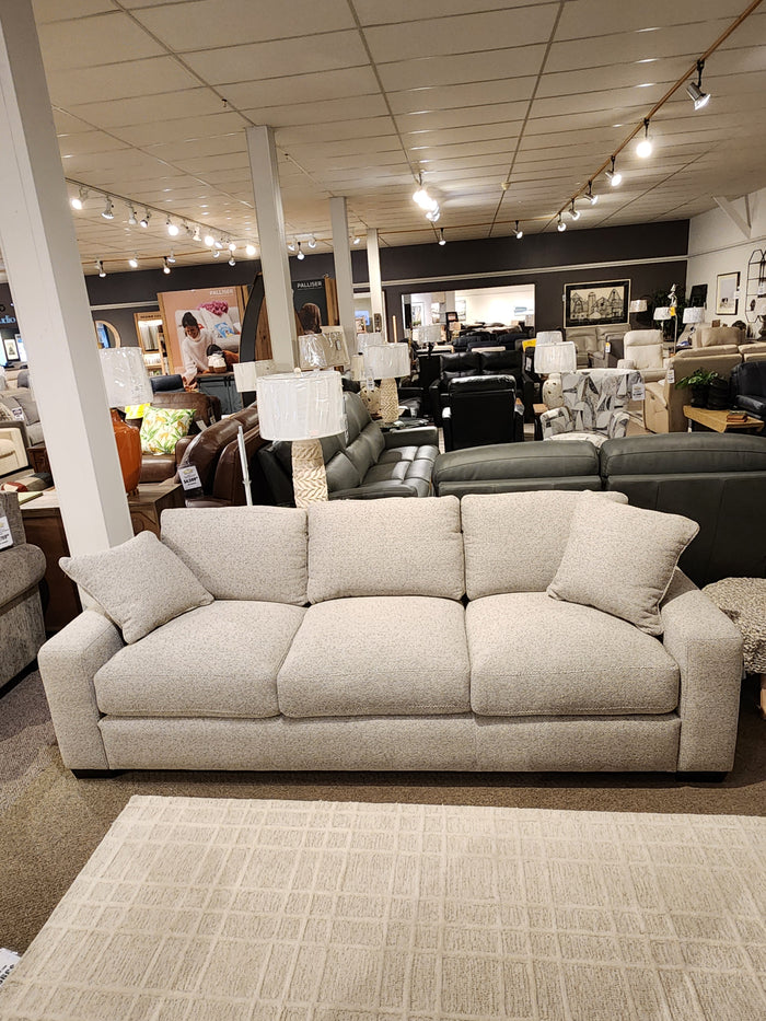 The Donald Choi Laguna Sofa has high-density foam seats, beige fabric, and two pillows, shown in a furniture showroom.