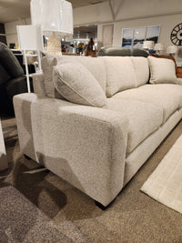 A beige Donald Choi Laguna Sofa with square arms and a high-density foam seat sits on a carpeted showroom floor.