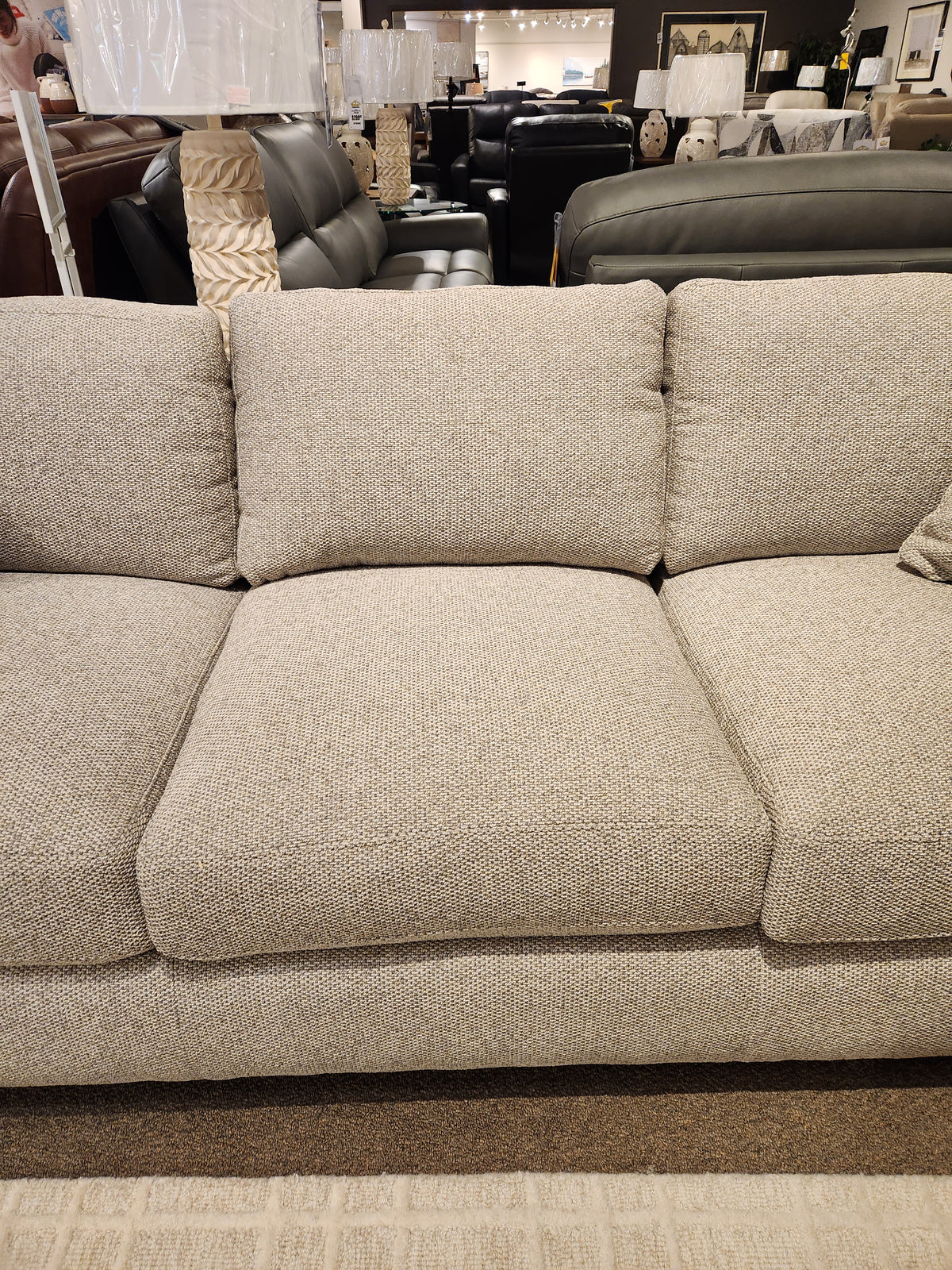 The Donald Choi Laguna Sofa features beige upholstery and a high-density foam seat, shown with couches and lamps in-store.