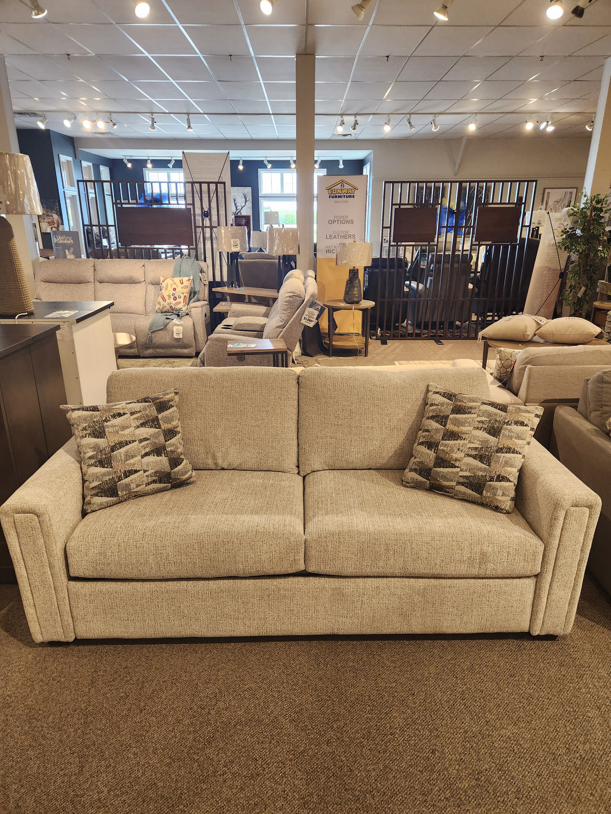 The Simmons Upholstery 9350 Queen Sofa Bed in beige with track arms and patterned pillows displayed in a showroom.
