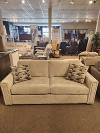 The Simmons Upholstery 9350 Queen Sofa Bed in beige with track arms and patterned pillows displayed in a showroom.
