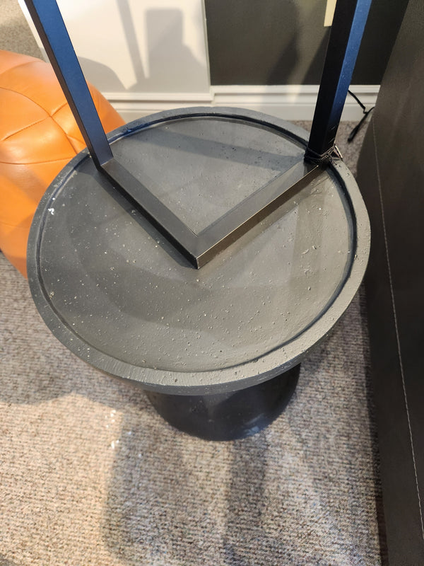 The Maru 15" Accent Table by Donald Choi is round, black, and sits beside a brown cushioned seat on carpet.