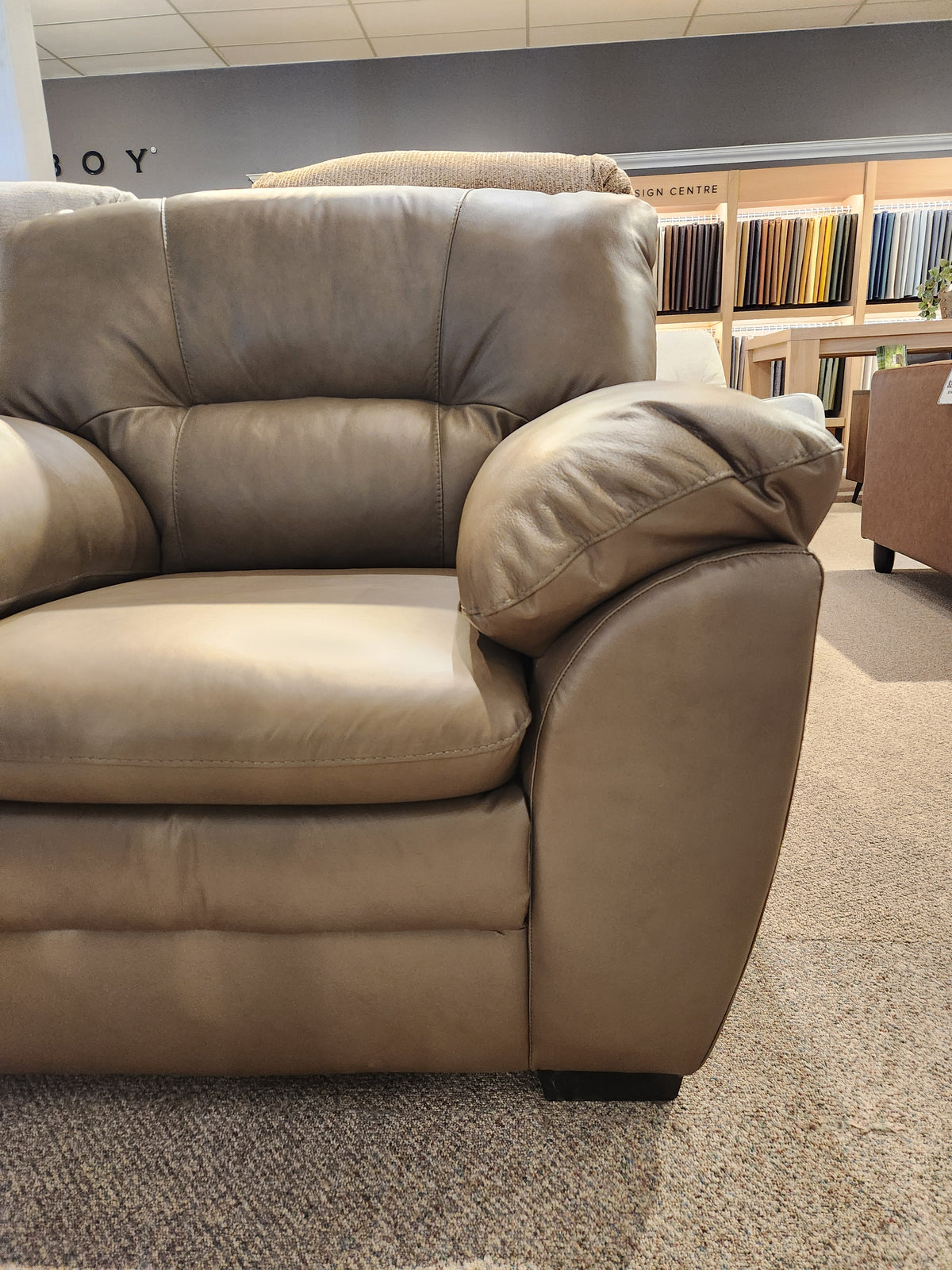 Close-up of the Palliser 77343 Amisk Chair in brown leather, with fabric samples displayed on the back wall.