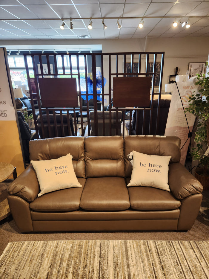 Palliser 77343 Amisk Sofa in brown leather with two "be here now" pillows, shown in a furniture showroom.