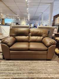 The Palliser 77343 Amisk Loveseat features brown leather and a high-resiliency foam seat, shown in a stylish showroom.