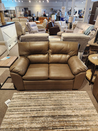 Palliser 77343 Amisk Loveseat in brown leather with high-resiliency foam sits behind a striped area rug.