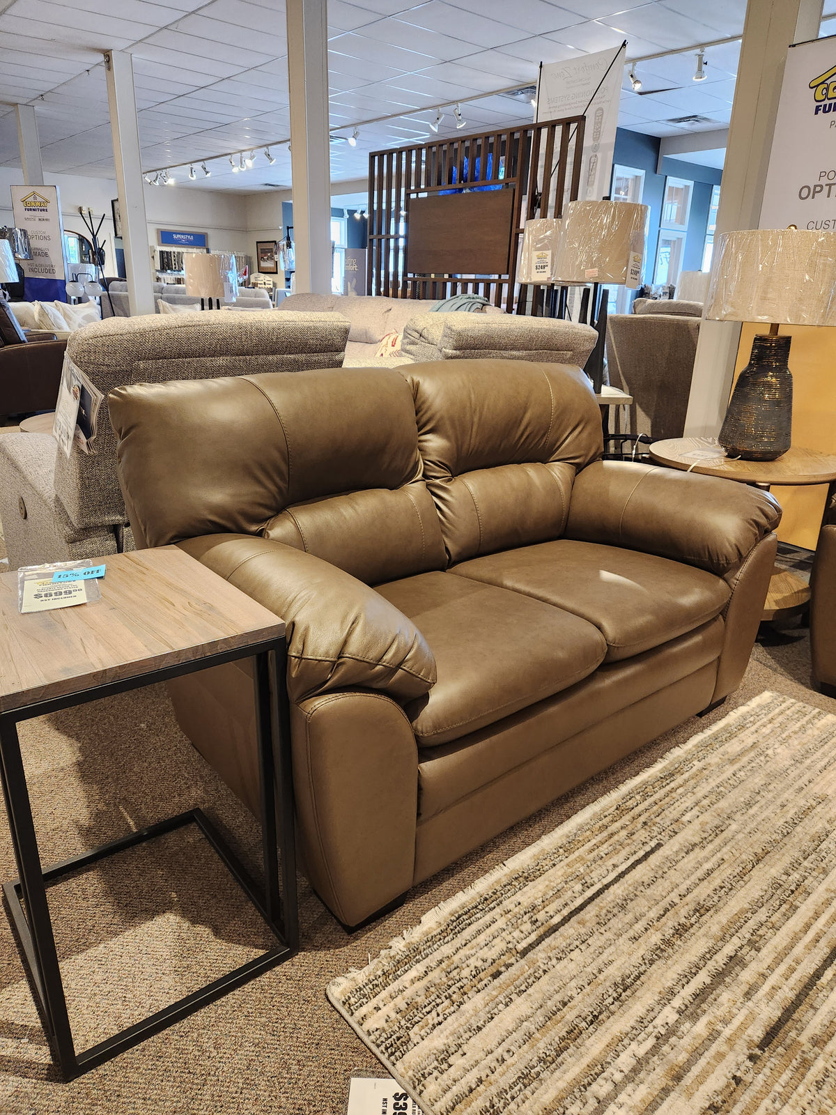 Palliser 77343 Amisk Loveseat in brown leather with high-resiliency foam seat, shown next to a wooden side table.