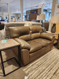 Palliser 77343 Amisk Loveseat in brown leather with high-resiliency foam seat, shown next to a wooden side table.