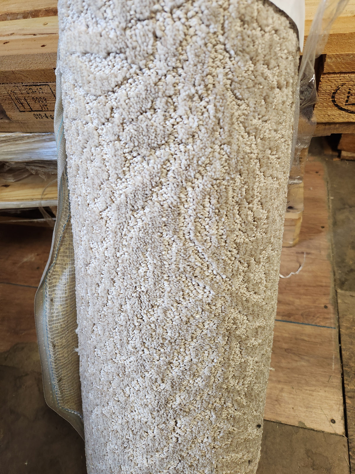 A Flooring CLEARANCE Carpet Remnant 12' X 2'6" in light beige and grey stands upright on a warehouse surface.