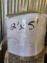 A Flooring CLEARANCE Carpet Remnant 12' x 5', taupe and low pile, is wrapped in plastic by corrugated metal.