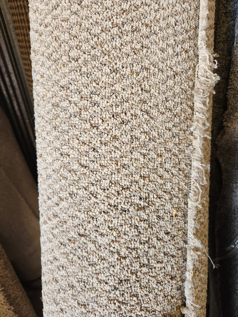 Close-up of Flooring CLEARANCE Carpet Remnant 8'10" x 4'10", low pile tan with textured surface and frayed right edge.