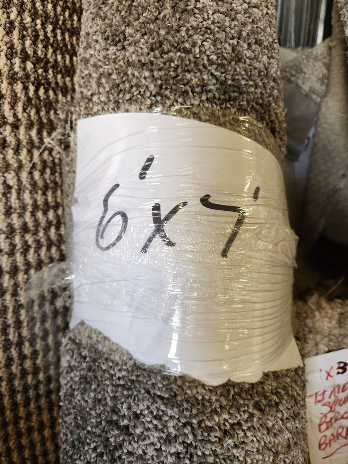 A Flooring CLEARANCE Carpet Remnant 6' X 7', rolled grey, labeled with handwritten marker, wrapped in plastic.