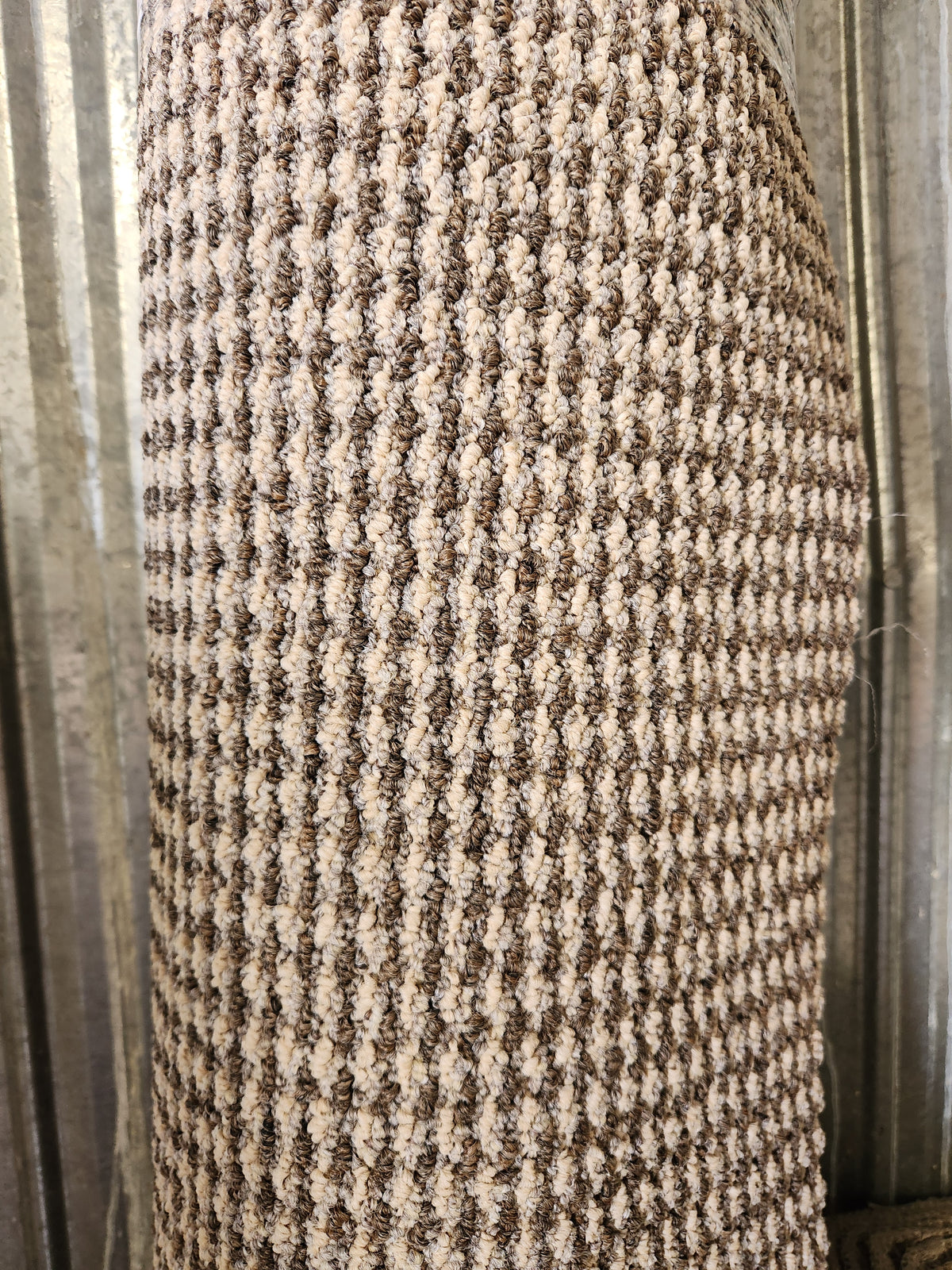 A close-up of a Flooring CLEARANCE Carpet Remnant 7' X 8', rolled and upright against a corrugated metal wall.
