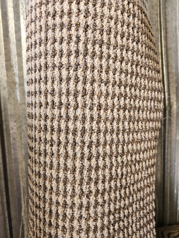 A close-up of a Flooring CLEARANCE Carpet Remnant 7' X 8', rolled and upright against a corrugated metal wall.