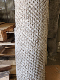 A Flooring CLEARANCE Carpet Remnant 12' X 3'9" in beige stands upright by wooden pallets in an industrial space.