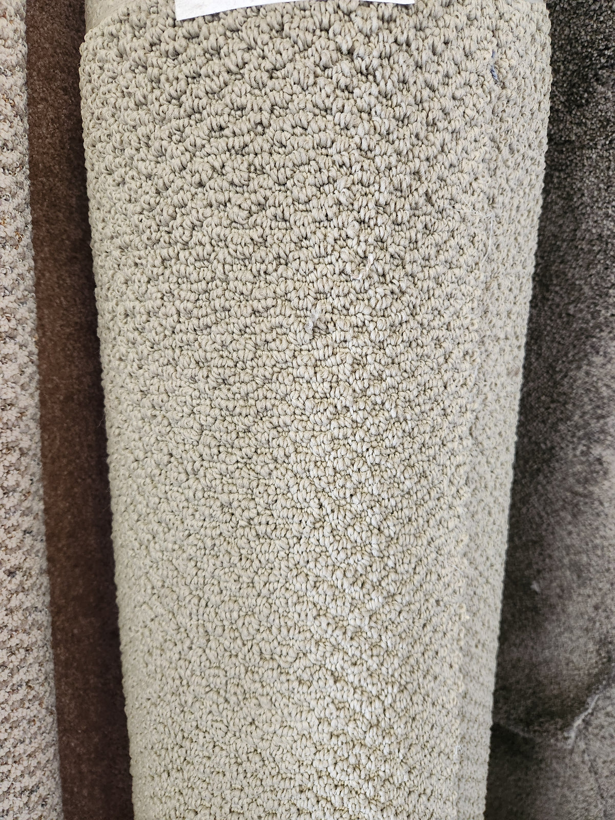 A close-up of Flooring CLEARANCE's Carpet Remnant 17'6" x 4'9", a beige, looped low-pile roll displayed upright.