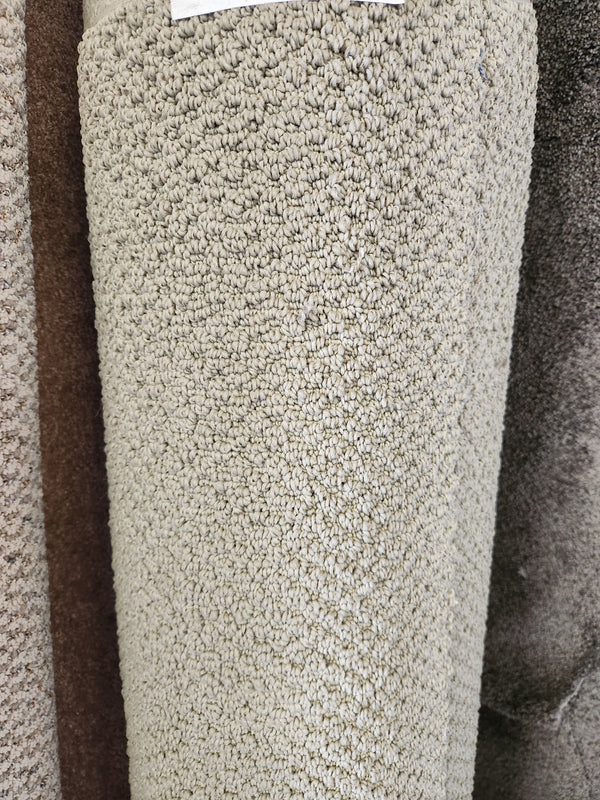 A close-up of Flooring CLEARANCE's Carpet Remnant 17'6" x 4'9", a beige, looped low-pile roll displayed upright.