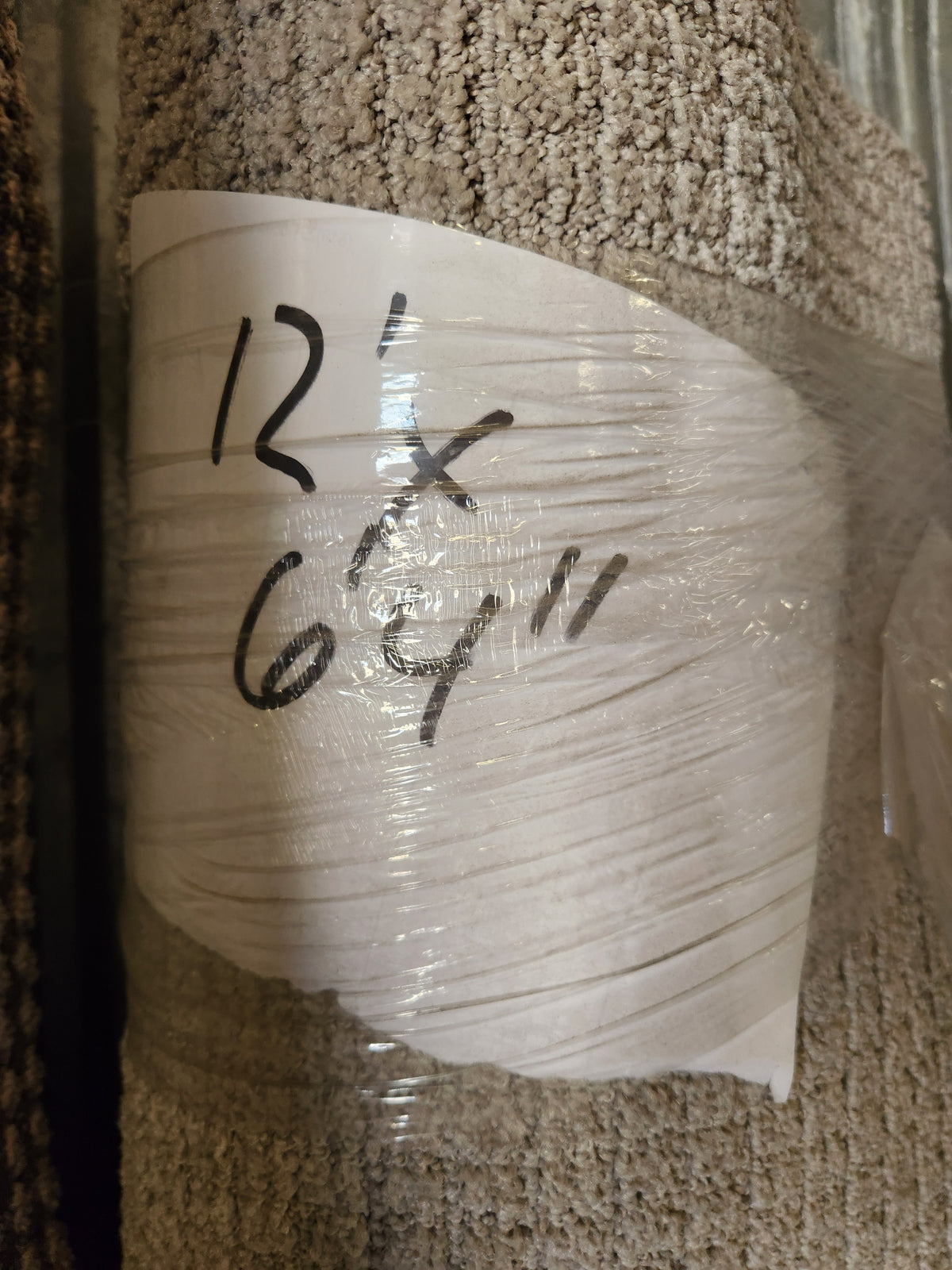 A Flooring CLEARANCE Carpet Remnant 12' X 6'4" in beige, low pile, wrapped in plastic.