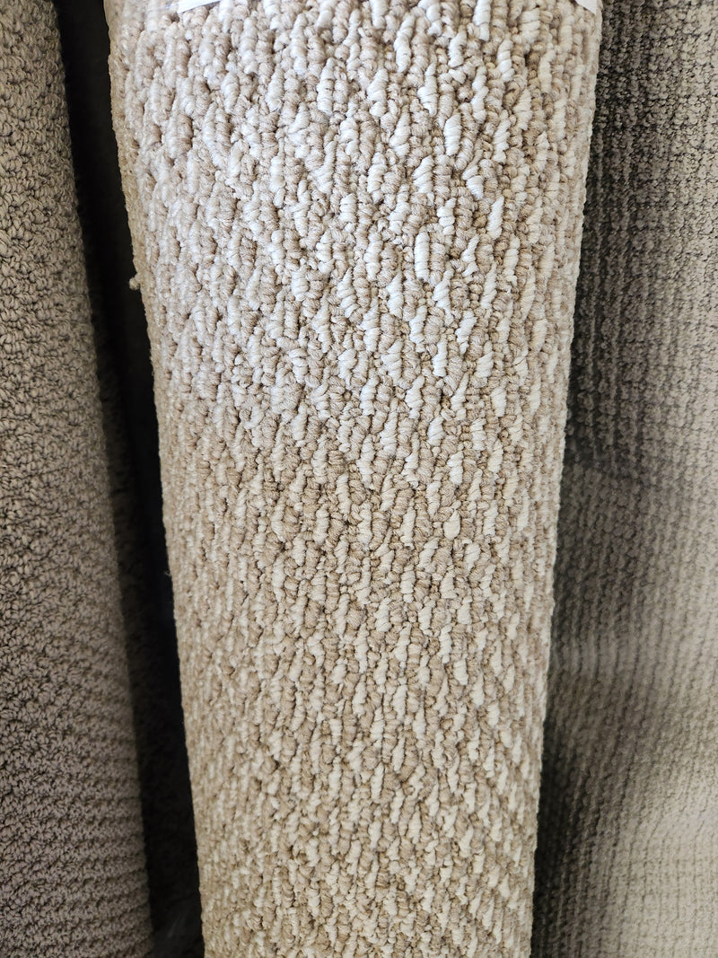 A close-up of Flooring CLEARANCE Carpet Remnant 5' X 7', light beige with visible low pile looped fibers, rolled upright.