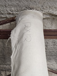 A Flooring CLEARANCE Carpet Remnant 12' X 12' in off-white rests on a rusted beam against a textured wall.