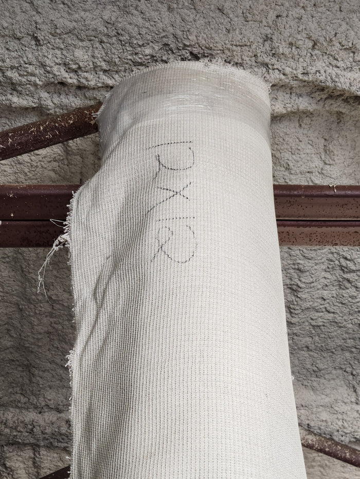 A Flooring CLEARANCE Carpet Remnant 12' X 12' in off-white rests on a rusted beam against a textured wall.
