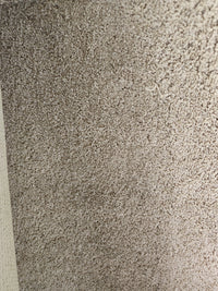 Close-up of Flooring CLEARANCE Carpet Remnant 12' X 12', beige medium pile, textured surface, wall edge on left.