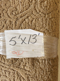 A Flooring CLEARANCE Carpet Remnant 5' X 13' in tan with handwritten label taped to the roll.