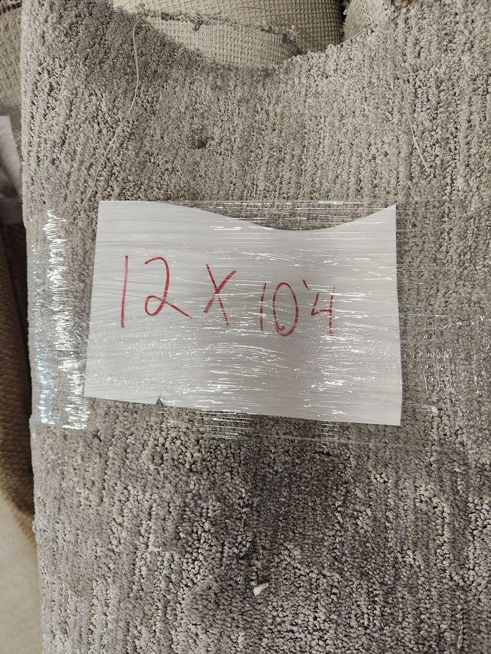 A "Carpet Remnant 12' X 10' 4"" by Flooring CLEARANCE is labeled with a handwritten sign on a light gray rug.
