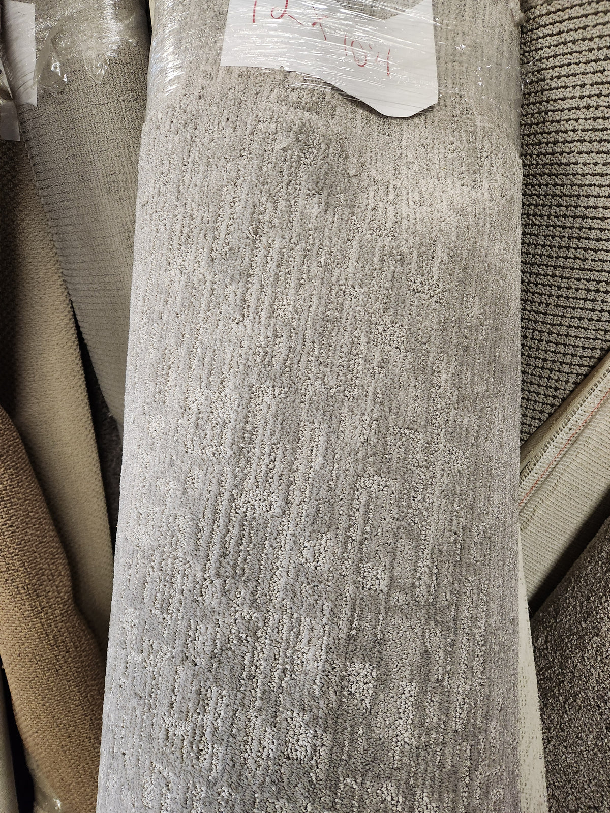 A Flooring CLEARANCE Carpet Remnant 12' X 10'4" in gray low pile stands among other rolls in store.