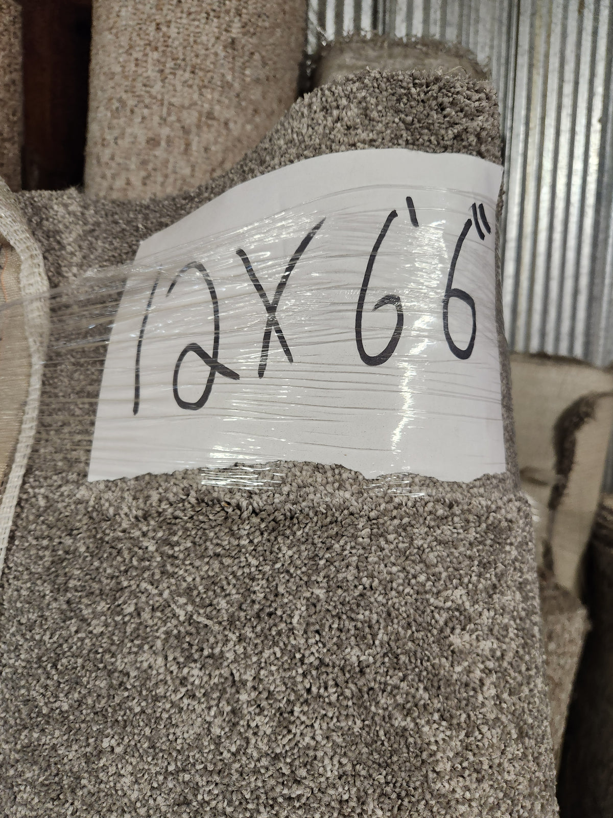 A Flooring CLEARANCE Carpet Remnant 12' x 6'6" in beige and medium pile is wrapped in plastic in storage.