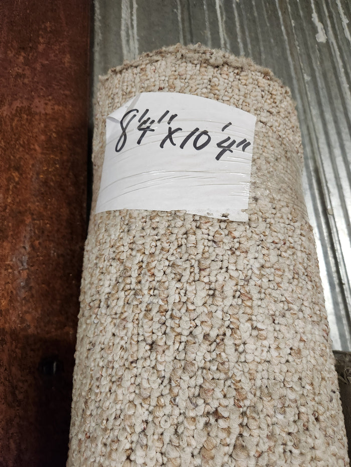 A Flooring CLEARANCE Carpet Remnant 8'4" x 10'4", light tan low loop pile, sits on a metal surface.