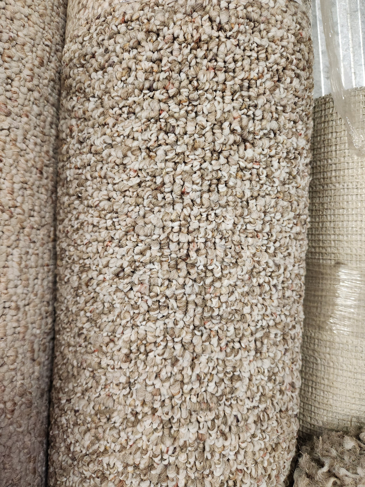 Close-up of Flooring CLEARANCE Carpet Remnant 6'10" X 9'6" with low loop pile, shown rolled near a woven rug.