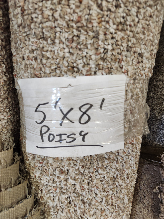 A rolled Carpet Remnant 5' X 8' by Flooring CLEARANCE with a handwritten sign taped to the beige carpet.
