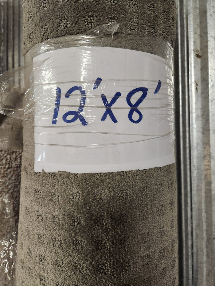 A rolled-up Flooring CLEARANCE Carpet Remnant 12' X 8', beige, low pile, wrapped in plastic with a handwritten sign.