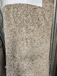 A close-up of the Flooring CLEARANCE Carpet Remnant 12' X 6', beige with medium pile, rolled against a metal background.
