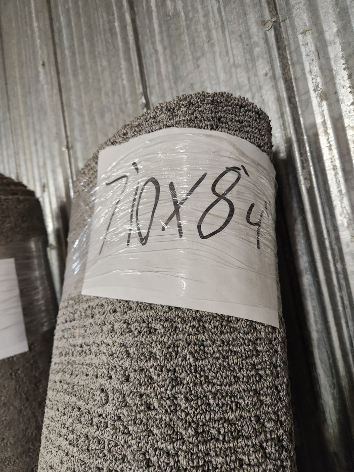 A Flooring CLEARANCE Carpet Remnant 7'10" x 8'4" in light grey leans against a corrugated metal wall.