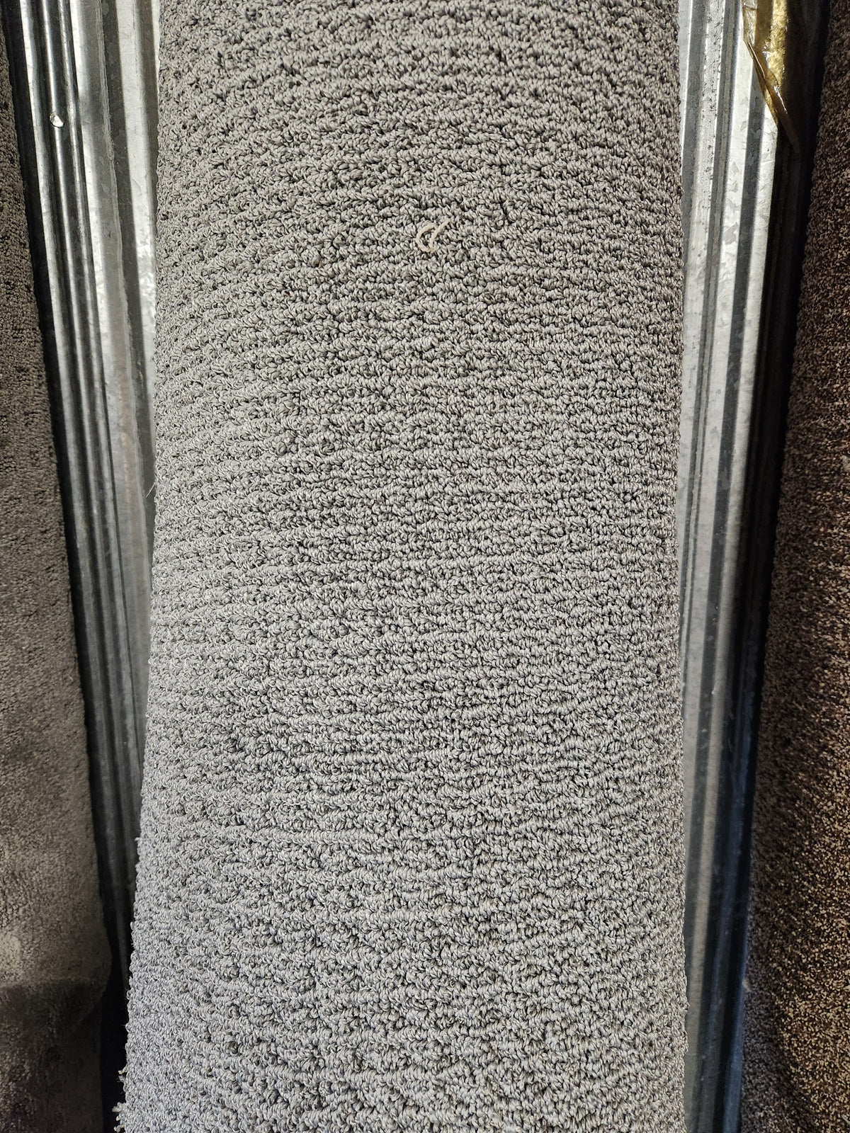 A close-up of a Flooring CLEARANCE Carpet Remnant 7'10" X 8'4" in Low Loop Pile light grey against a metal background.