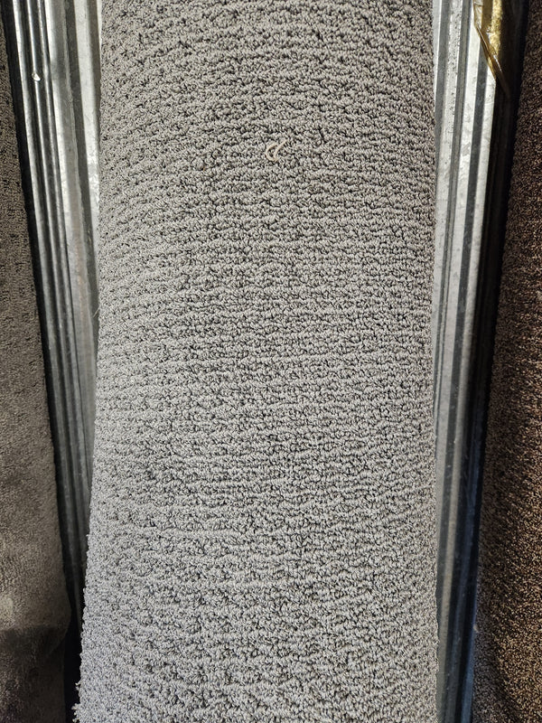 A close-up of a Flooring CLEARANCE Carpet Remnant 7'10" X 8'4" in Low Loop Pile light grey against a metal background.