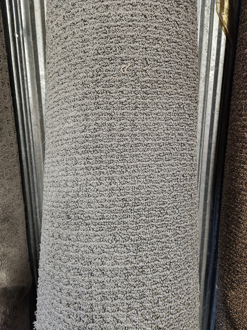 A close-up of a Flooring CLEARANCE Carpet Remnant 7'10" X 8'4" in Low Loop Pile light grey against a metal background.