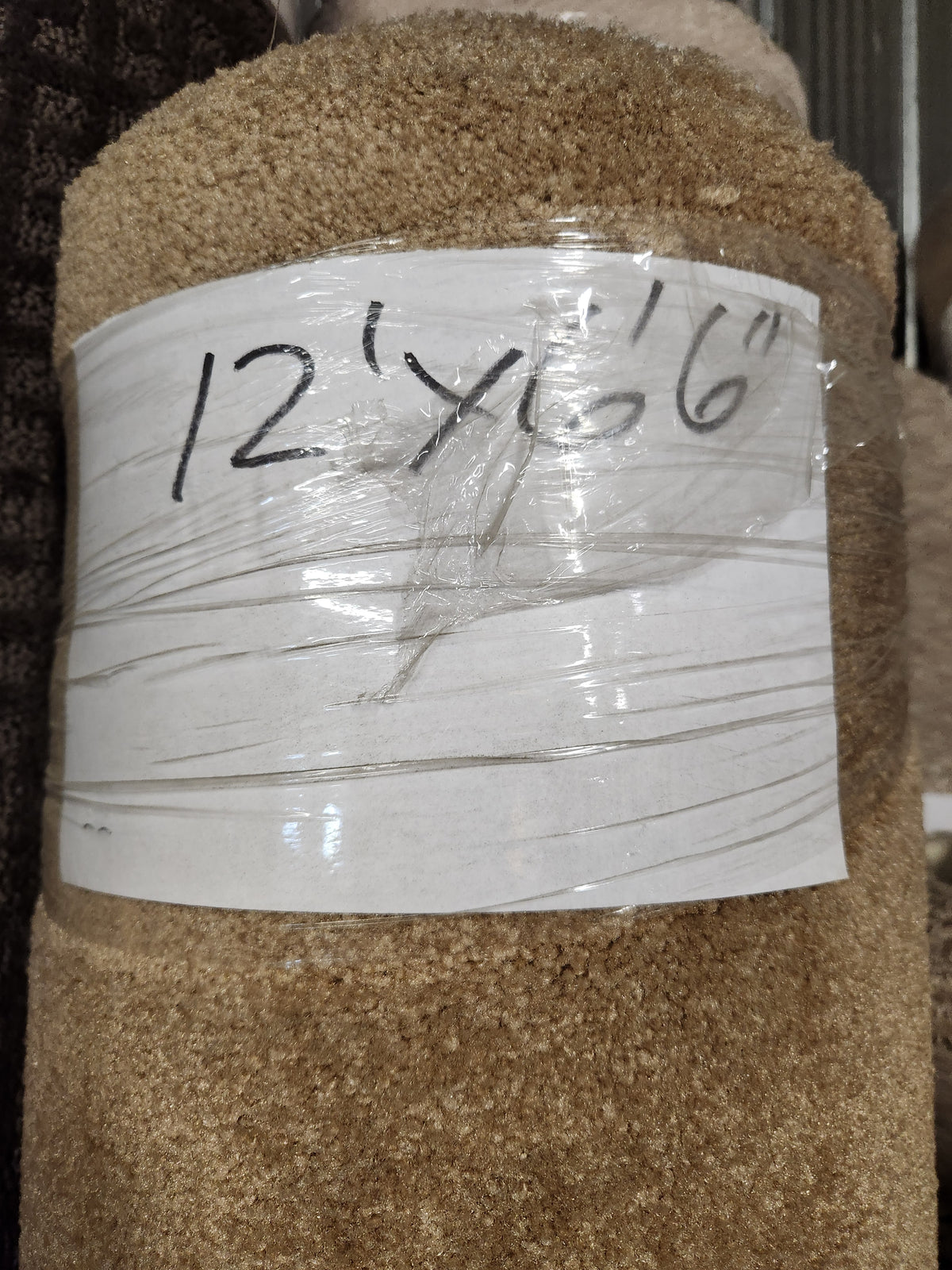 A Flooring CLEARANCE Carpet Remnant 12' x 6'6" in beige, wrapped in plastic with handwritten label.