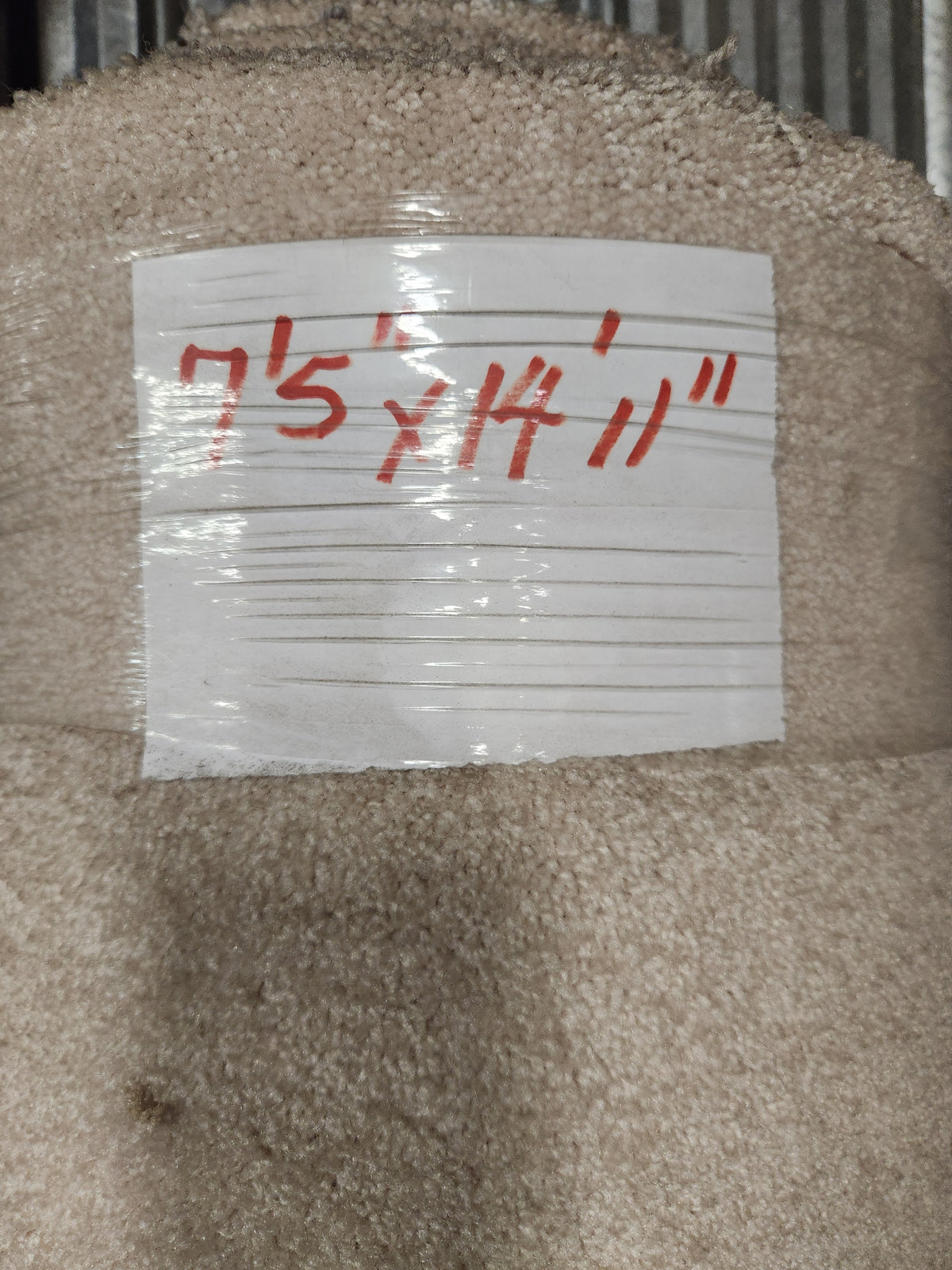 A roll of Flooring CLEARANCE Carpet Remnant 7'5" x 14'11", light beige, medium pile, labeled in red on white tape.