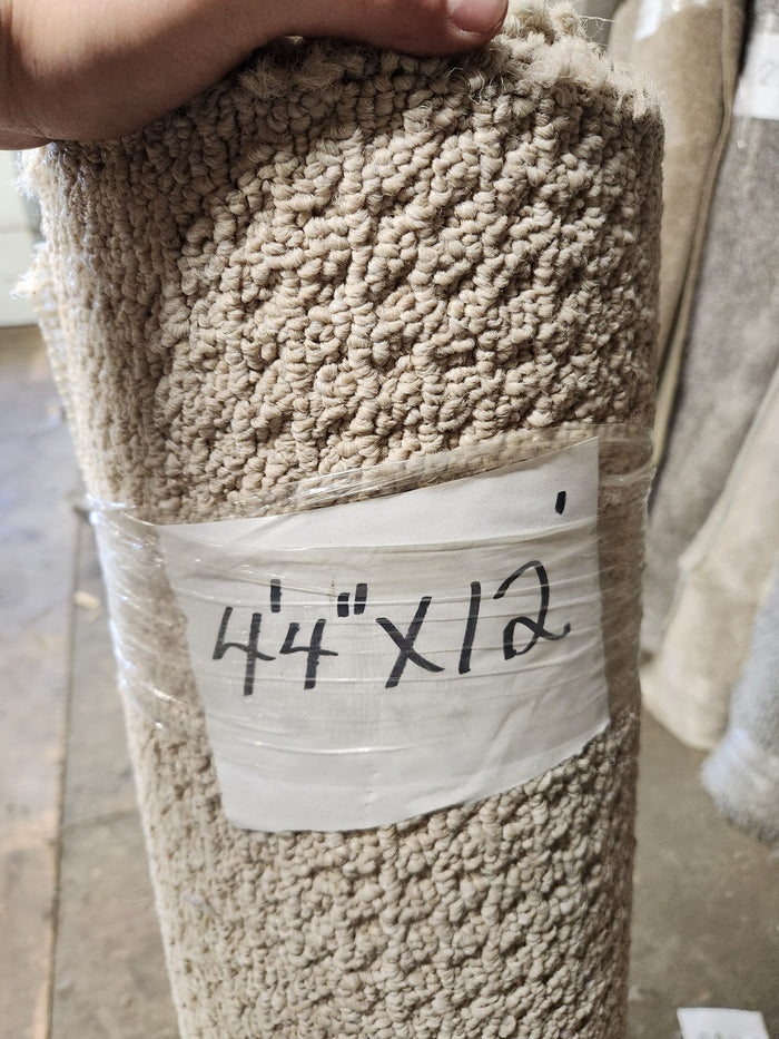 A rolled beige Carpet Remnant 4'4" x 12" by Flooring CLEARANCE with a handwritten size label attached.