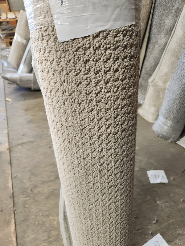A Flooring CLEARANCE Carpet Remnant 4'4" X 12', beige and textured, stands upright on a warehouse floor with labels.